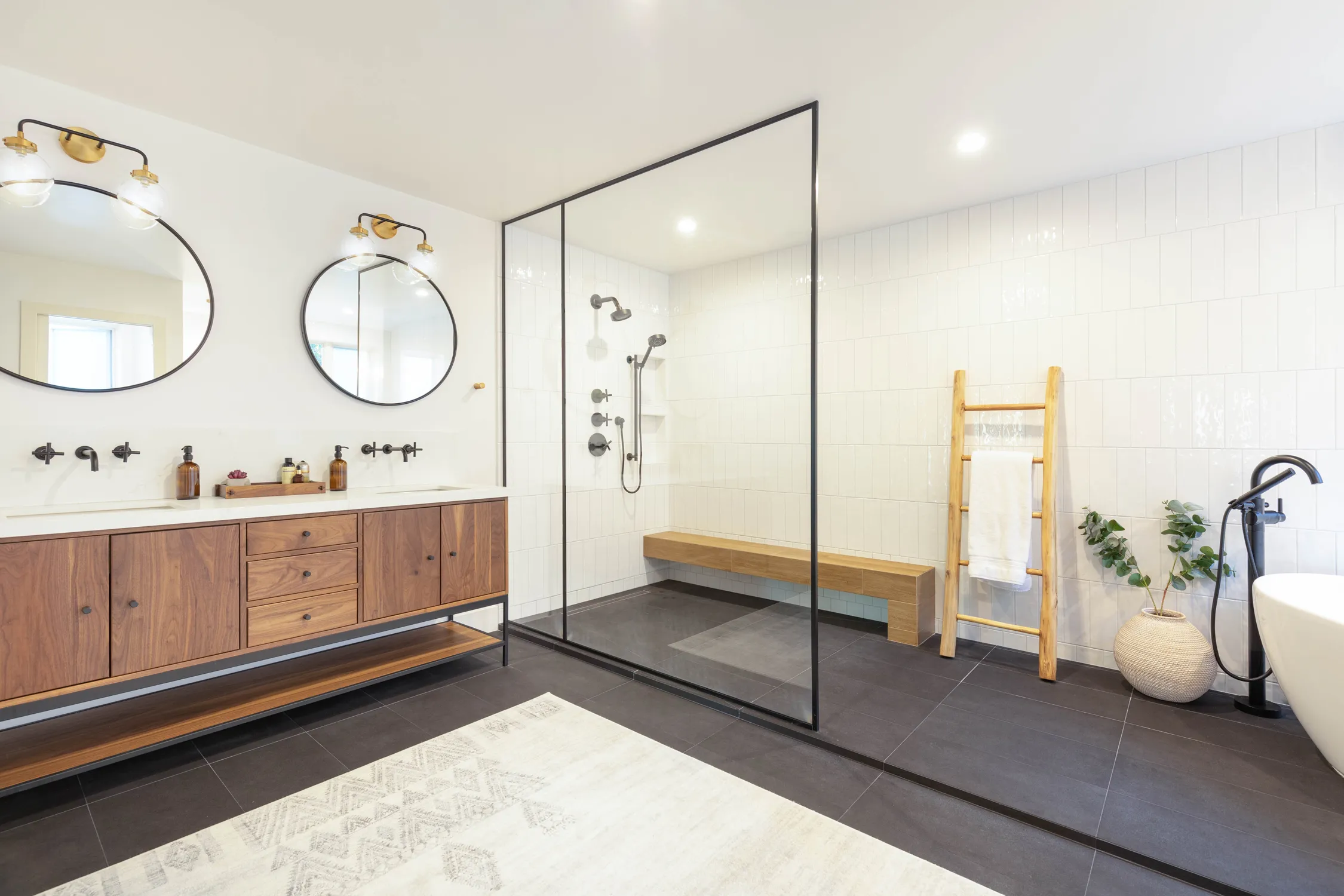Wood double vanity beside a black-tile glass shower