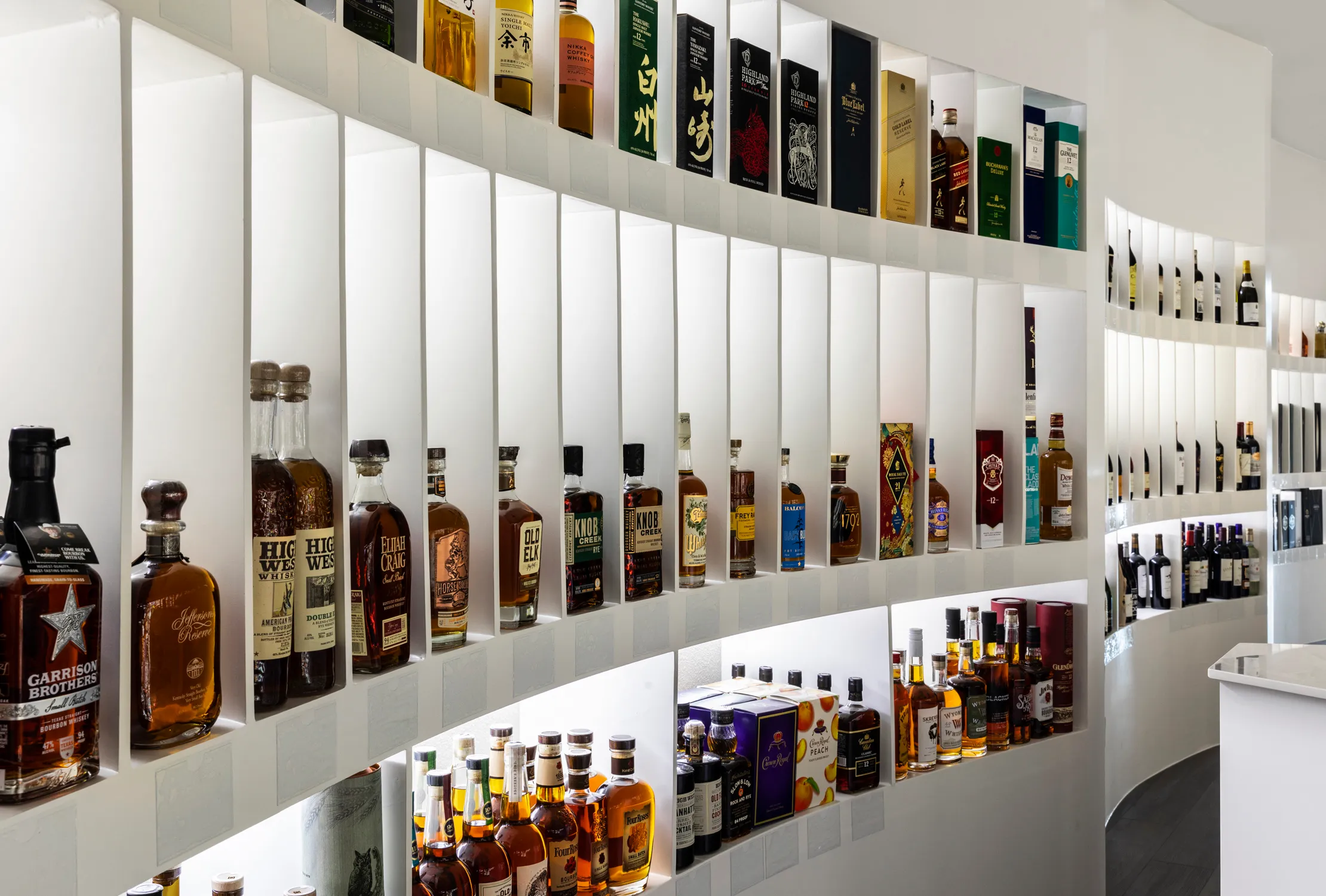 Backlit bottle shelving along a curved liquor store aisle