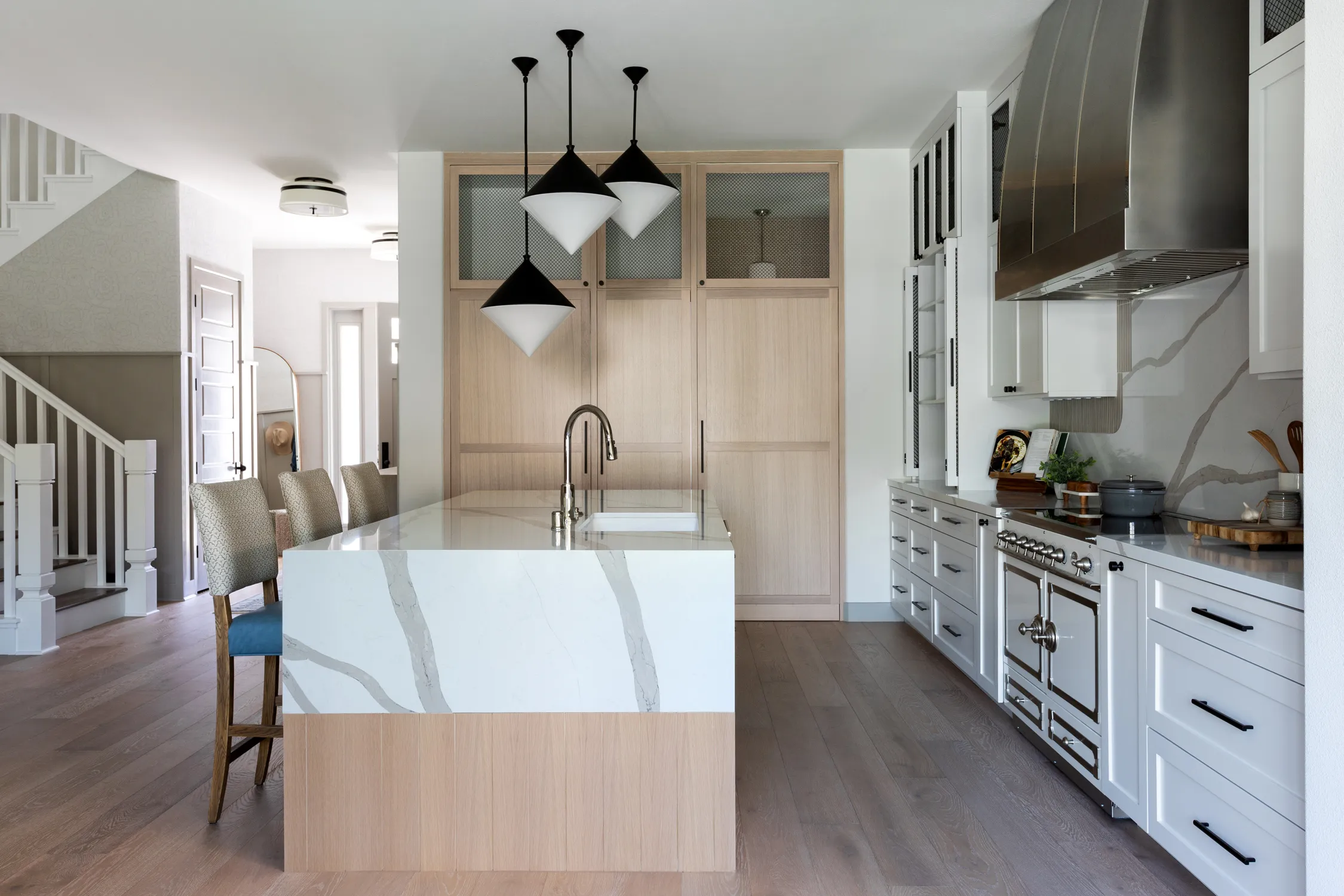 White waterfall island beside a marble backsplash and pendant lights