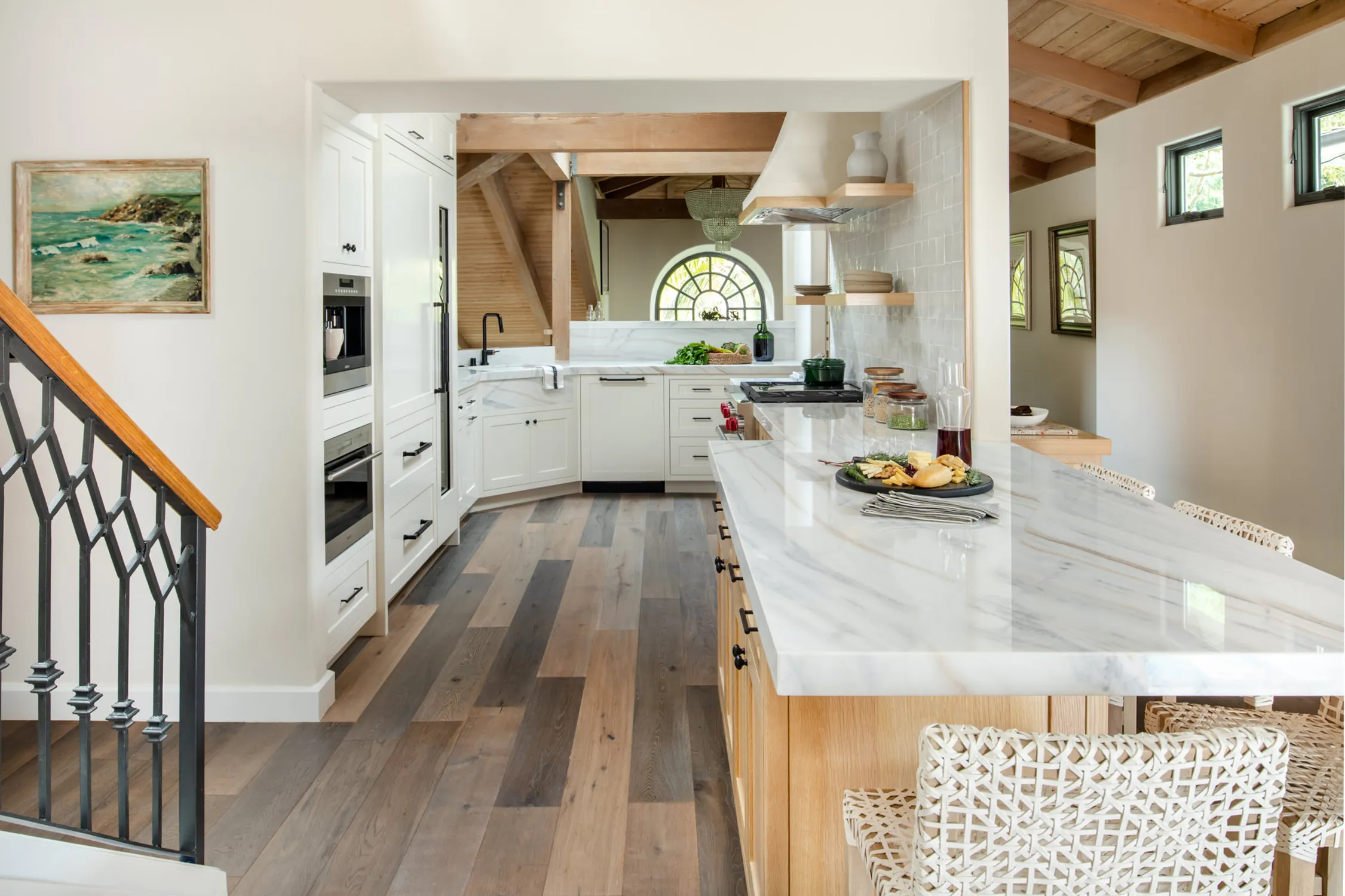 White kitchen with marble island beneath exposed wood beams