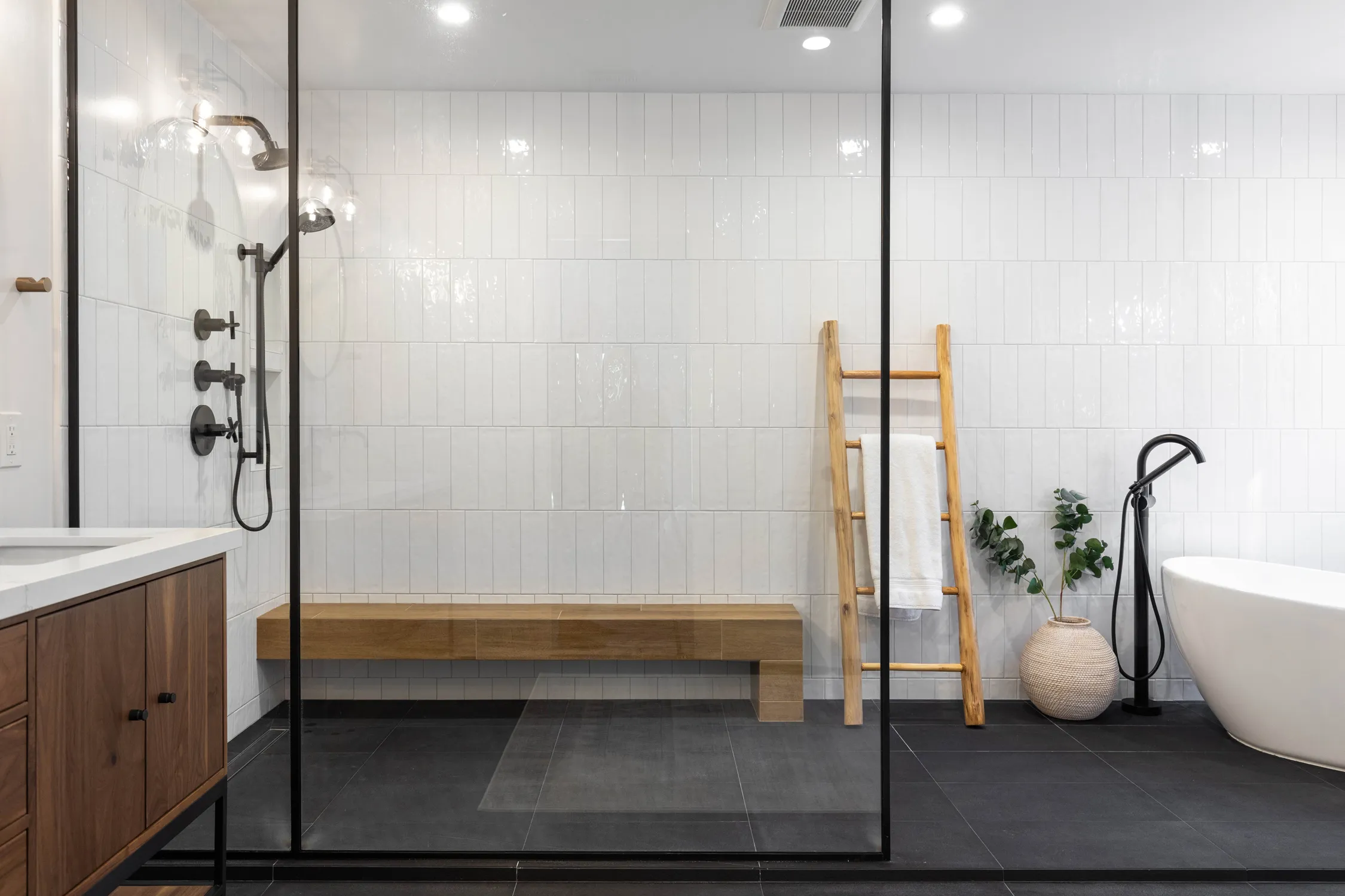 Glass shower with black tile floor and freestanding tub