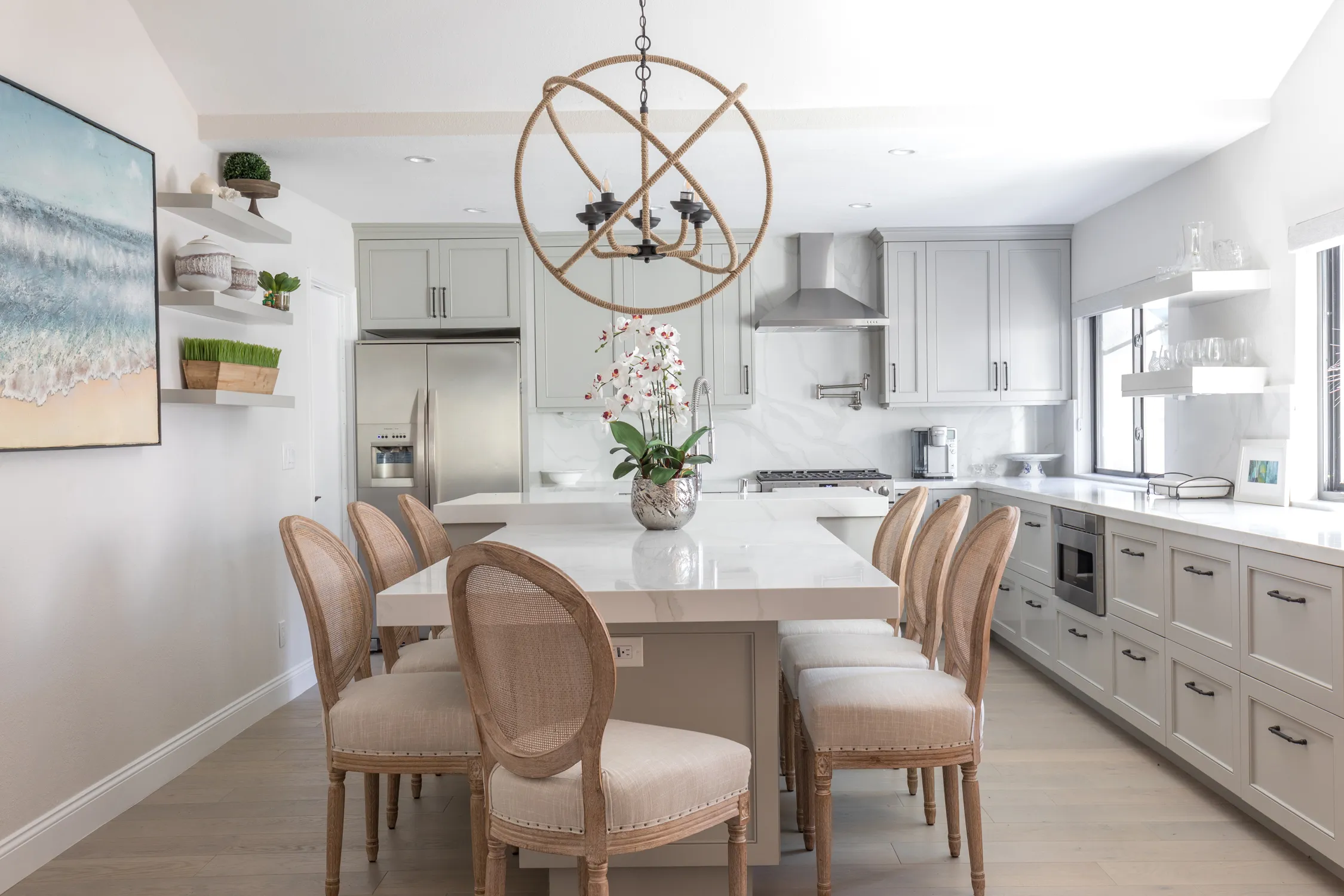 White kitchen with cane-backed chairs beneath a rope globe chandelier