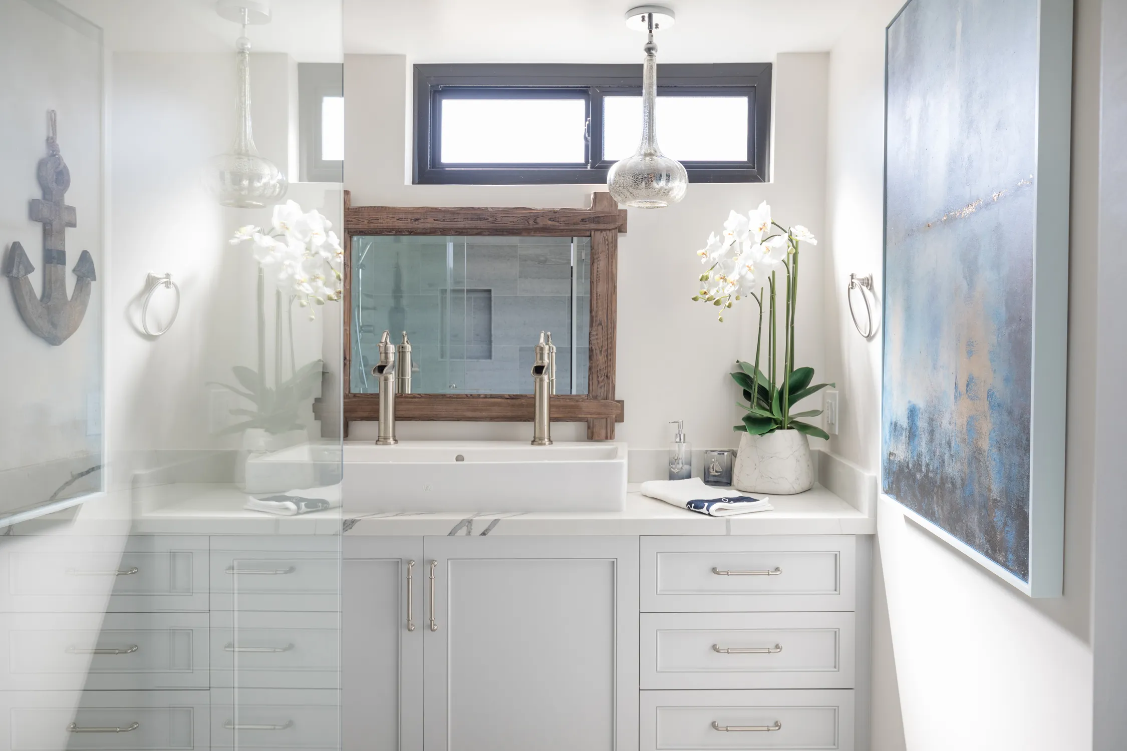 White vanity below dark-trimmed window and nautical artwork