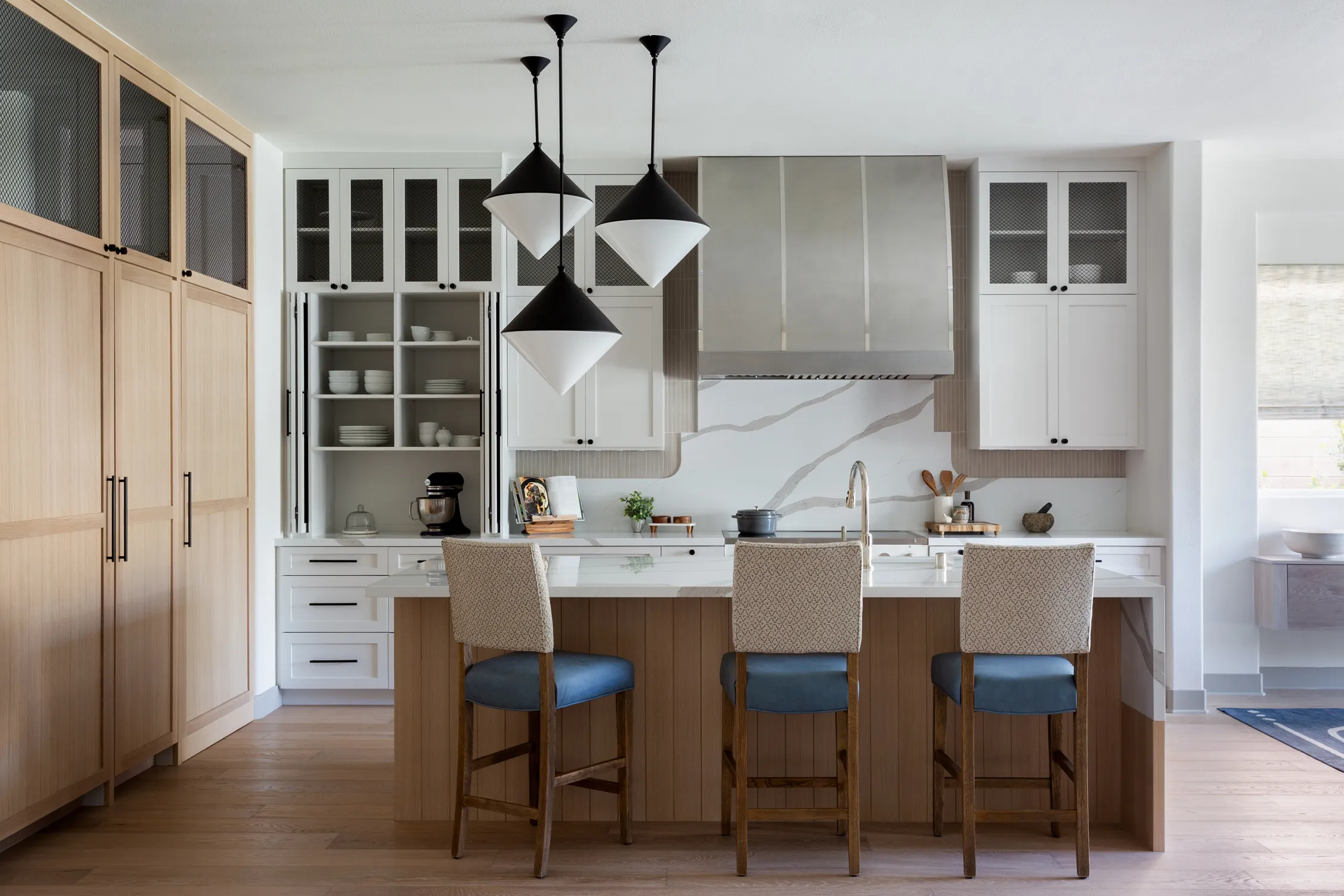 Light-wood kitchen with black pendant lights and island stools