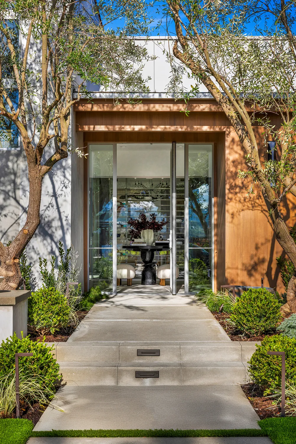 Glass entry framed by olive trees and wood cladding
