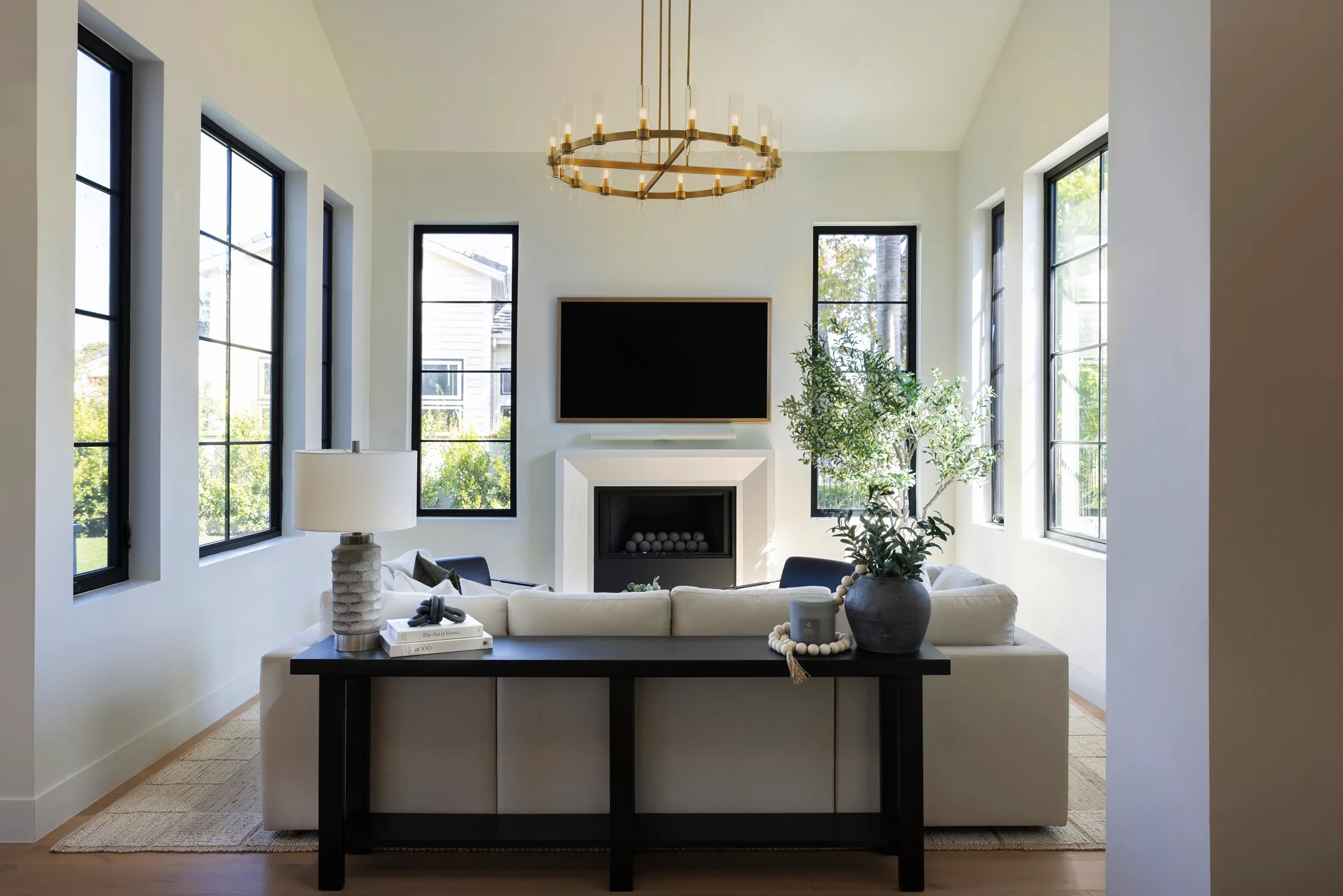 Vaulted living room with brass chandelier and black-framed windows.