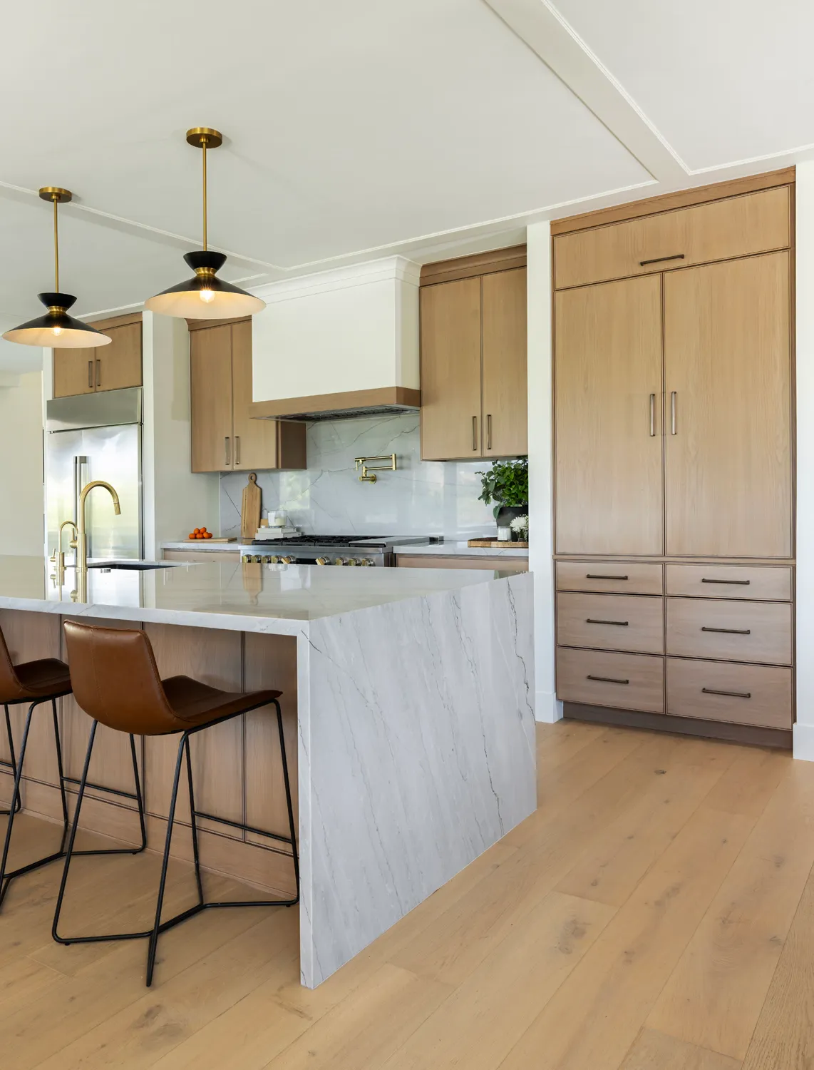 Kitchen with waterfall island, wood cabinetry and brass fixtures.