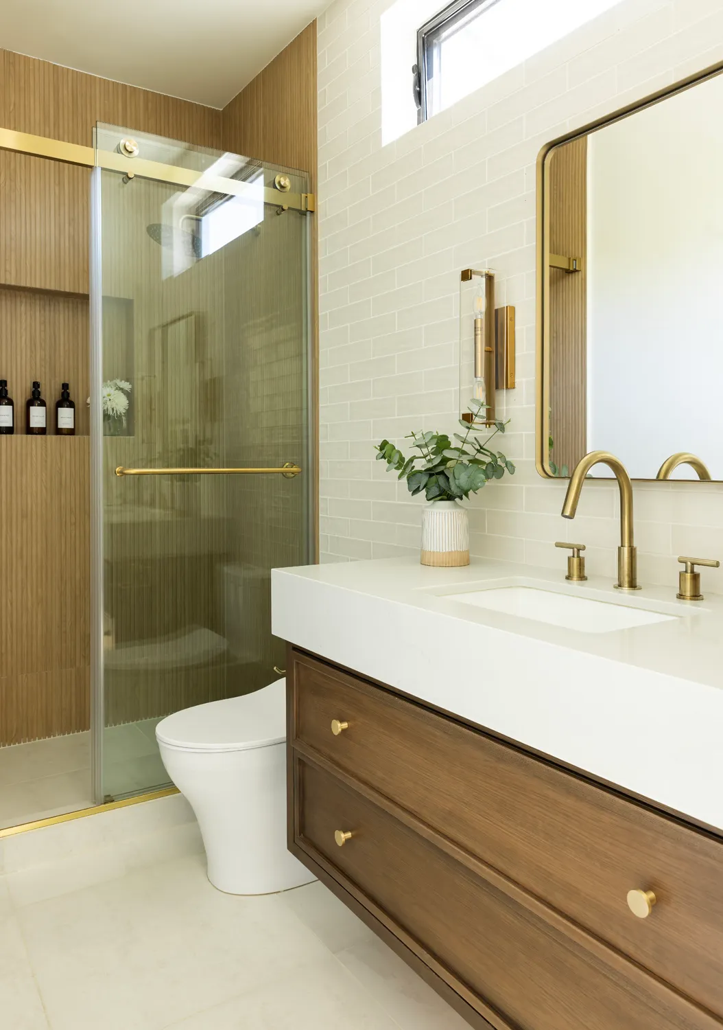 Remodeled bathroom with wood vanity, brass fixtures, and glass shower