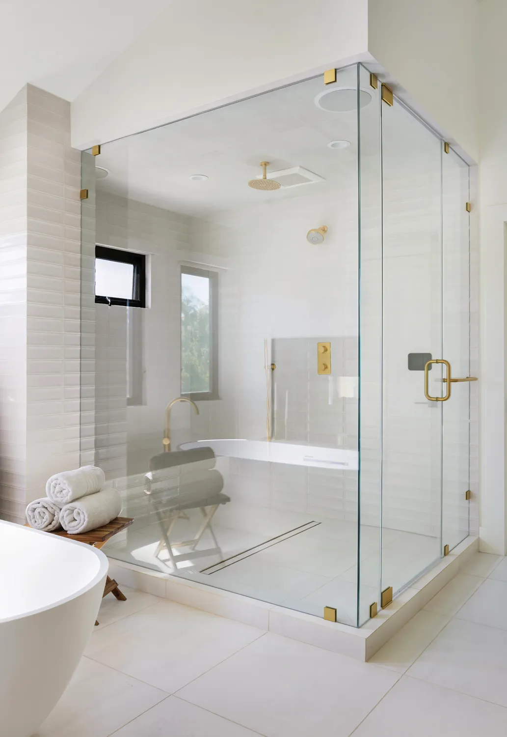 Glass-enclosed shower with white tile, freestanding tub, and brass fixtures