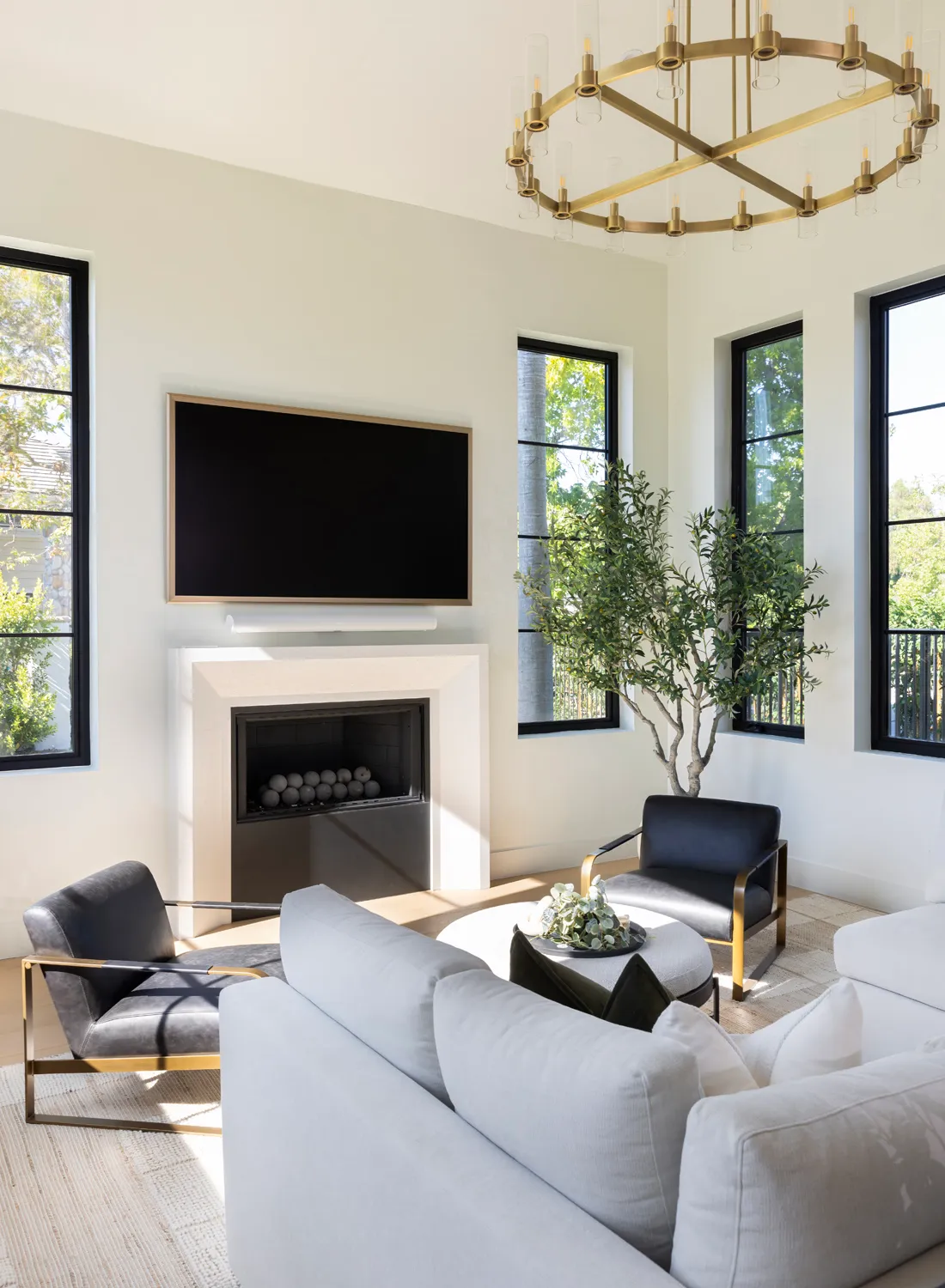 Bright living room with fireplace, brass chandelier, and black-framed windows