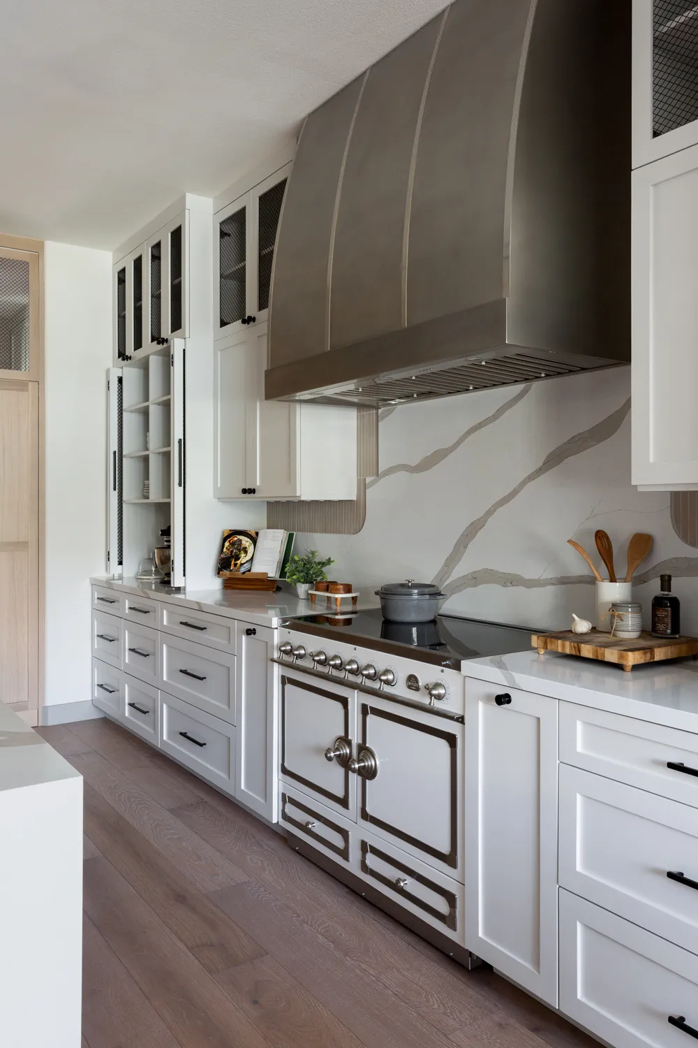 White kitchen with stainless-steel range, large hood, and marble backsplash